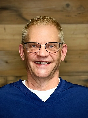 Chiropractor Mark Glesener Smiling In Front Of Wooden Wall